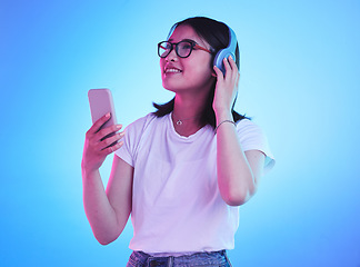 Image showing Woman, student and phone with headphones listening to music, techno streaming and radio on blue background. Person, gen z or youth audio, electronics and mobile subscription in neon light and studio