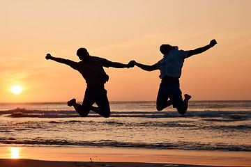 Image showing Beach sunset, shadow silhouette and couple jump, holding hands and having fun, bonding and enjoy nature freedom. Sky, tropical ocean sea and excited people celebrate outdoor travel on spring vacation