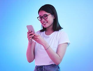 Image showing Phone, typing an Asian woman on social media with mobile app, internet or web isolated in a studio blue background. Connection, cellphone and young female chatting with smile for communication