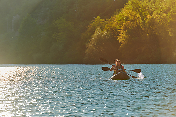 Image showing A young couple enjoying an idyllic kayak ride in the middle of a beautiful river surrounded by forest greenery in sunset time