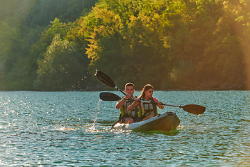 Image showing A young couple enjoying an idyllic kayak ride in the middle of a beautiful river surrounded by forest greenery in sunset time