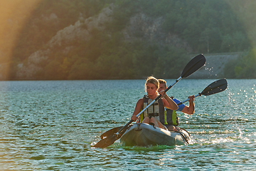 Image showing A young couple enjoying an idyllic kayak ride in the middle of a beautiful river surrounded by forest greenery in sunset time