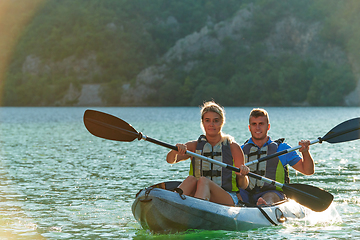 Image showing A young couple enjoying an idyllic kayak ride in the middle of a beautiful river surrounded by forest greenery in sunset time