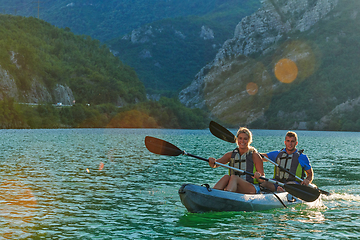 Image showing A young couple enjoying an idyllic kayak ride in the middle of a beautiful river surrounded by forest greenery in sunset time