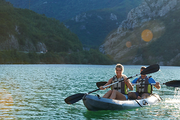 Image showing A young couple enjoying an idyllic kayak ride in the middle of a beautiful river surrounded by forest greenery in sunset time