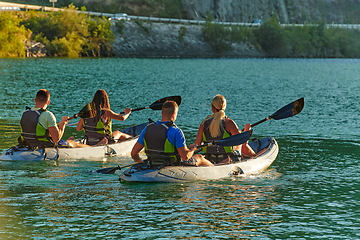 Image showing A group of friends enjoying fun and kayaking exploring the calm river, surrounding forest and large natural river canyons during an idyllic sunset.