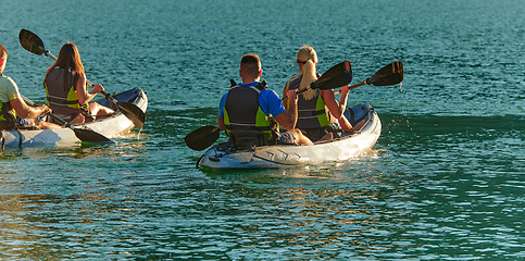 Image showing A group of friends enjoying fun and kayaking exploring the calm river, surrounding forest and large natural river canyons during an idyllic sunset.