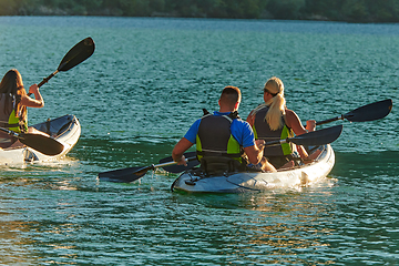 Image showing A group of friends enjoying fun and kayaking exploring the calm river, surrounding forest and large natural river canyons during an idyllic sunset.