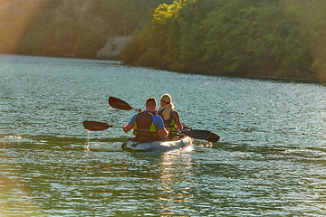 Image showing A young couple enjoying an idyllic kayak ride in the middle of a beautiful river surrounded by forest greenery in sunset time