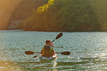 Image showing A young couple enjoying an idyllic kayak ride in the middle of a beautiful river surrounded by forest greenery in sunset time