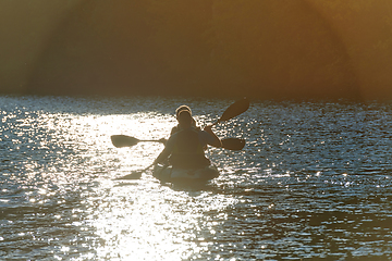 Image showing A young couple enjoying an idyllic kayak ride in the middle of a beautiful river surrounded by forest greenery in sunset time