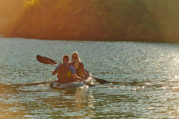 Image showing A young couple enjoying an idyllic kayak ride in the middle of a beautiful river surrounded by forest greenery in sunset time