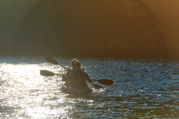 Image showing A young couple enjoying an idyllic kayak ride in the middle of a beautiful river surrounded by forest greenery in sunset time