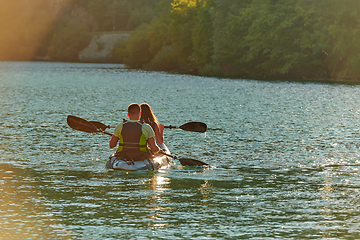 Image showing A young couple enjoying an idyllic kayak ride in the middle of a beautiful river surrounded by forest greenery in sunset time