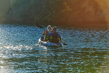 Image showing A young couple enjoying an idyllic kayak ride in the middle of a beautiful river surrounded by forest greenery in sunset time