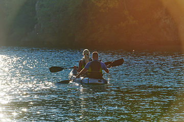 Image showing A young couple enjoying an idyllic kayak ride in the middle of a beautiful river surrounded by forest greenery in sunset time