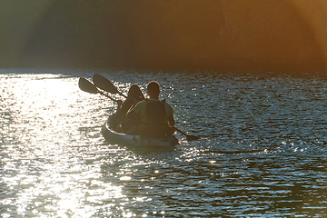 Image showing A young couple enjoying an idyllic kayak ride in the middle of a beautiful river surrounded by forest greenery in sunset time