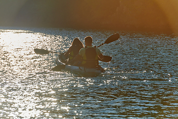 Image showing A young couple enjoying an idyllic kayak ride in the middle of a beautiful river surrounded by forest greenery in sunset time