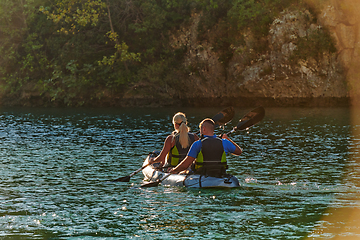 Image showing A young couple enjoying an idyllic kayak ride in the middle of a beautiful river surrounded by forest greenery in sunset time