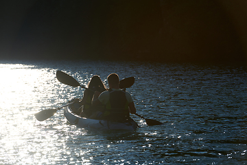 Image showing A young couple enjoying an idyllic kayak ride in the middle of a beautiful river surrounded by forest greenery in sunset time