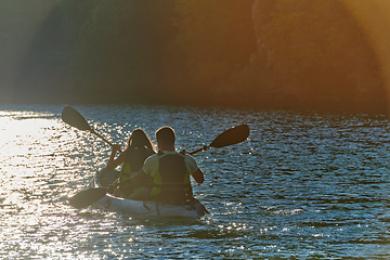 Image showing A young couple enjoying an idyllic kayak ride in the middle of a beautiful river surrounded by forest greenery in sunset time