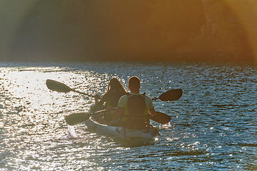 Image showing A young couple enjoying an idyllic kayak ride in the middle of a beautiful river surrounded by forest greenery in sunset time