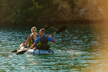 Image showing A young couple enjoying an idyllic kayak ride in the middle of a beautiful river surrounded by forest greenery in sunset time