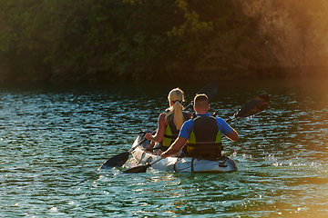 Image showing A young couple enjoying an idyllic kayak ride in the middle of a beautiful river surrounded by forest greenery in sunset time