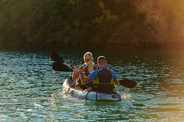 Image showing A young couple enjoying an idyllic kayak ride in the middle of a beautiful river surrounded by forest greenery in sunset time