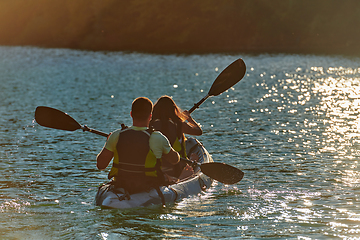 Image showing A young couple enjoying an idyllic kayak ride in the middle of a beautiful river surrounded by forest greenery in sunset time