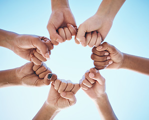 Image showing Hands, fist and people in circle with low angle for trust, solidarity and motivation on blue sky background. Power, hands and friends collaboration with hope, community and support of goal or mission