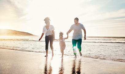 Image showing Playing, beach and family walking together on a vacation, adventure or holiday together for bonding. Sunset, having fun and girl child with her mother and father on the sand by ocean on weekend trip.