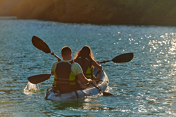 Image showing A young couple enjoying an idyllic kayak ride in the middle of a beautiful river surrounded by forest greenery in sunset time