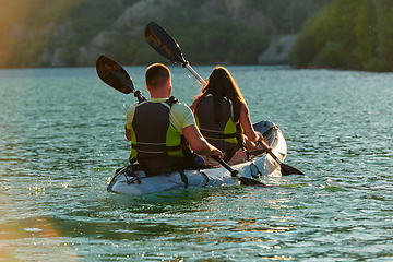 Image showing A young couple enjoying an idyllic kayak ride in the middle of a beautiful river surrounded by forest greenery in sunset time