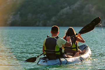 Image showing A young couple enjoying an idyllic kayak ride in the middle of a beautiful river surrounded by forest greenery in sunset time