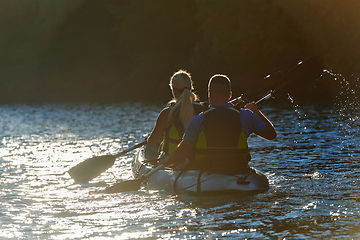 Image showing A young couple enjoying an idyllic kayak ride in the middle of a beautiful river surrounded by forest greenery in sunset time