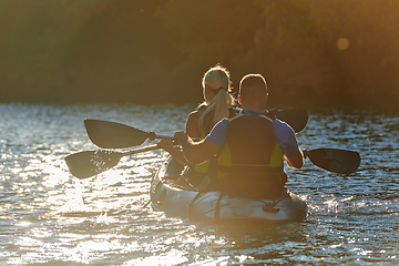 Image showing A young couple enjoying an idyllic kayak ride in the middle of a beautiful river surrounded by forest greenery in sunset time