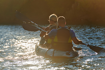 Image showing A young couple enjoying an idyllic kayak ride in the middle of a beautiful river surrounded by forest greenery in sunset time