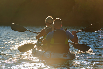 Image showing A young couple enjoying an idyllic kayak ride in the middle of a beautiful river surrounded by forest greenery in sunset time