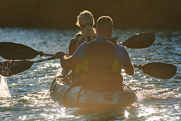 Image showing A young couple enjoying an idyllic kayak ride in the middle of a beautiful river surrounded by forest greenery in sunset time