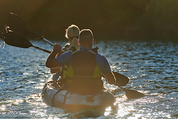 Image showing A young couple enjoying an idyllic kayak ride in the middle of a beautiful river surrounded by forest greenery in sunset time