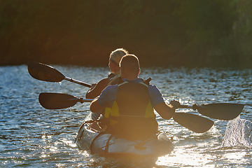 Image showing A young couple enjoying an idyllic kayak ride in the middle of a beautiful river surrounded by forest greenery in sunset time