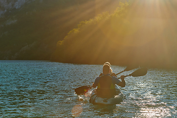 Image showing A young couple enjoying an idyllic kayak ride in the middle of a beautiful river surrounded by forest greenery in sunset time