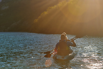 Image showing A young couple enjoying an idyllic kayak ride in the middle of a beautiful river surrounded by forest greenery in sunset time