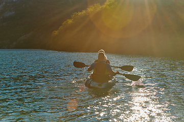 Image showing A young couple enjoying an idyllic kayak ride in the middle of a beautiful river surrounded by forest greenery in sunset time