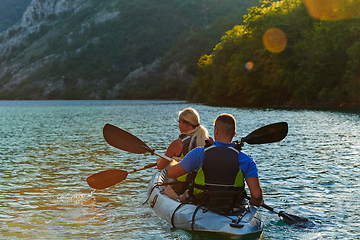 Image showing A young couple enjoying an idyllic kayak ride in the middle of a beautiful river surrounded by forest greenery in sunset time