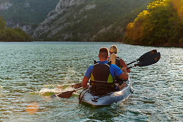 Image showing A young couple enjoying an idyllic kayak ride in the middle of a beautiful river surrounded by forest greenery in sunset time