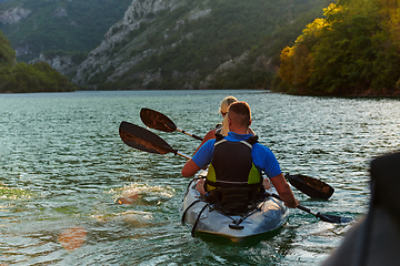 Image showing A young couple enjoying an idyllic kayak ride in the middle of a beautiful river surrounded by forest greenery in sunset time