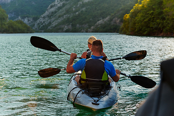 Image showing A young couple enjoying an idyllic kayak ride in the middle of a beautiful river surrounded by forest greenery in sunset time