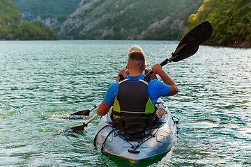 Image showing A young couple enjoying an idyllic kayak ride in the middle of a beautiful river surrounded by forest greenery in sunset time